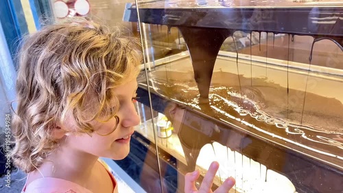  Young girl looking at a large industrial chocolate fountain in a shop window.