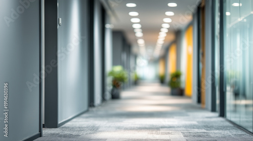 A long and modern office hallway with gray walls and carpeted floor leading to a blurred background with natural light