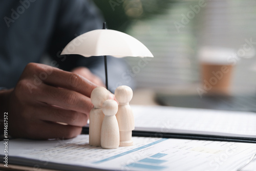 Billede på lærred Life insurance concept showing family protection with wooden figures under umbrella on financial documents