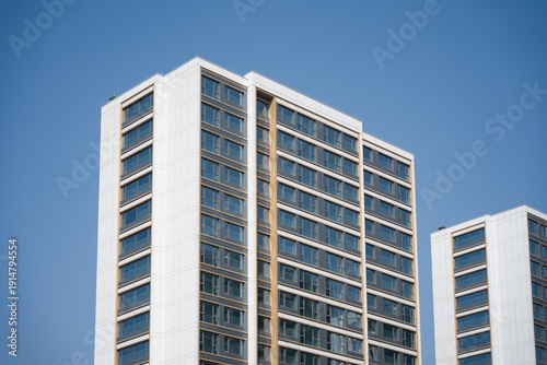 Modern white high-rise residential building with clean lines and glass windows against a clear blue sky