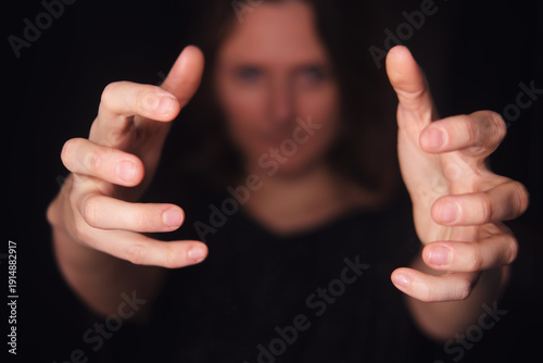 Fotografie Woman with outstretcched hands on a dark background holding or grabbing an imaginary object or interacting with virtual reality and technology