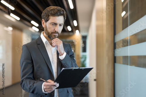 Bilde på lerret Confident businessman in a formal suit intently reviewing documents on a clipboa