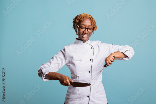 Quadro su tela Smiling professional cook stands confidently against isolated background, holding knife and meat fork