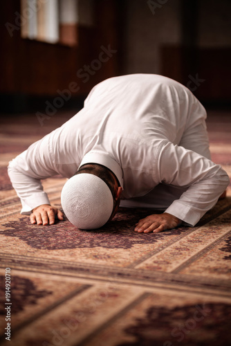 Muslim man in white clothing performing sujood prostration during salah on patterned prayer rug indoors showing islamic faith devotion spiritual worship and daily religious practice in mosque