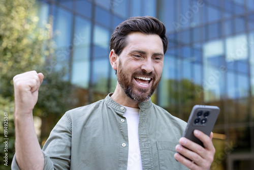 Εκτύπωση καμβά Smiling man feeling excited and triumphing, receiving excellent news on his mobi