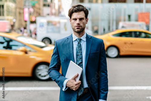Handsome businessman walking in Manhattan, carrying digital tablet