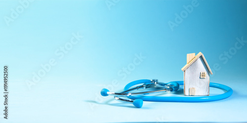 Miniature house and stethoscope on blue background with copy space