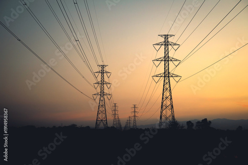 Silhouette of high-voltage electric transmission towers and power lines against a beautiful sunset sky with orange and purple hues.