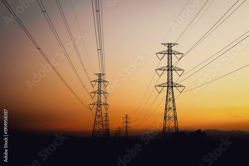 Schilderij op canvas Silhouette of high-voltage electric transmission towers and power lines against a beautiful sunset sky with orange and purple hues