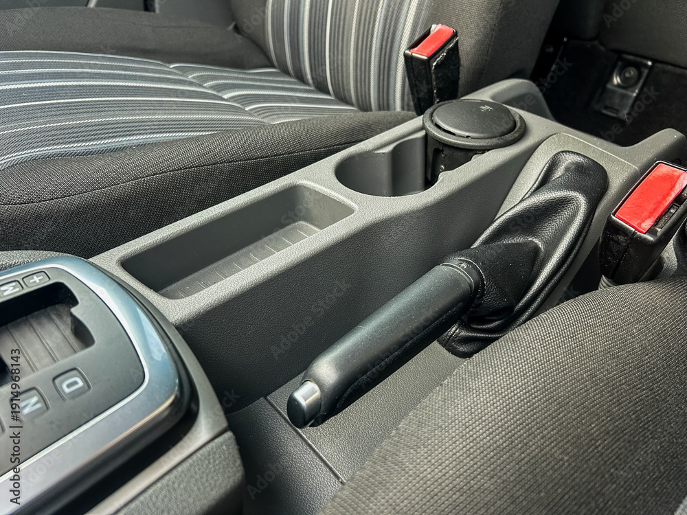 Obraz premium Car interior features center console with gear shift, cup holder, and seatbelt fasteners in a vehicle parked indoors during the day