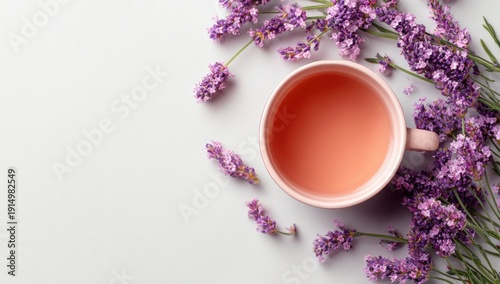 Overhead view of a pale pink mug filled with light pink herbal tea, surrounded by sprigs of fresh lavender blossoms on a light gray background