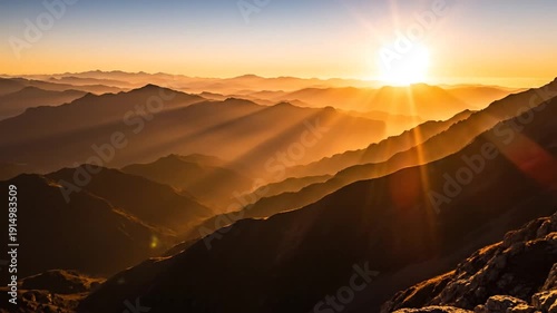 Dramatic sunrise over a vast mountain range with golden light rays and atmospheric haze