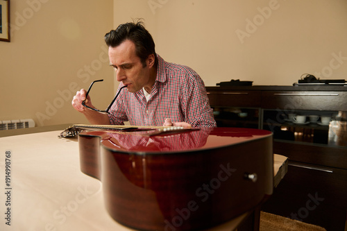 Fotografie Man Adjusting Guitar Strings at Home Table - Guitar Maintenance and Repair