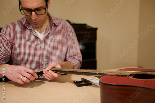 Schilderij op canvas Man Changing Guitar Strings at Table - Guitar Maintenance and Repair Practice