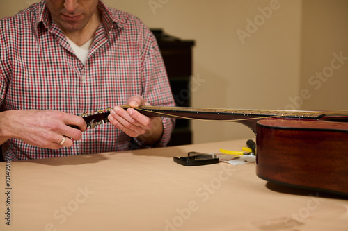 Fotografie Man Changing Guitar Strings at Table - Guitar Maintenance and Repair Hands-On