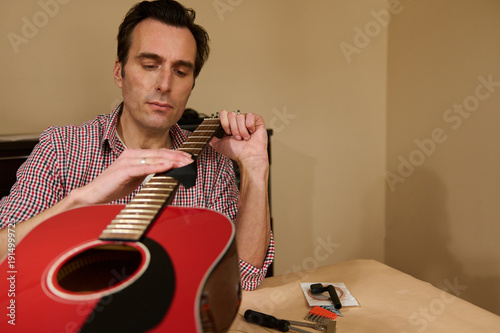 Man Adjusting Guitar Strings During Maintenance and Repair of Red Acoustic Guitar