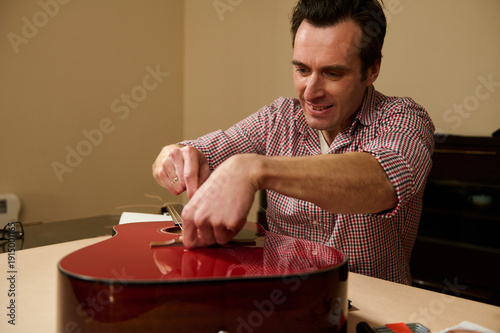 Fotografie Man Changing Guitar Strings and Adjusting Bridge - Guitar Maintenance and Repair