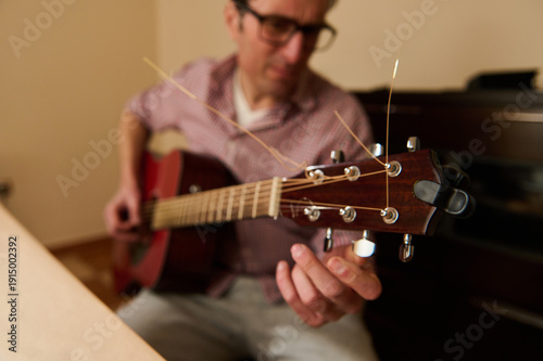 Obraz na plátně Man Adjusting Guitar Strings at Home — Guitar Maintenance and Repair Concept