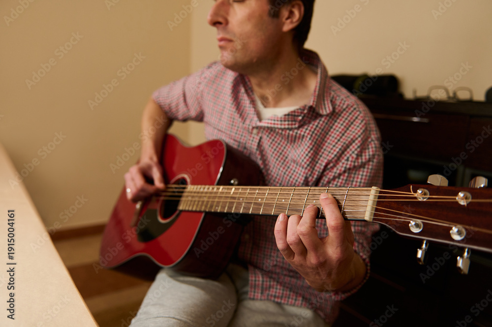 Obraz premium Man Adjusting and Changing Guitar Strings on Red Acoustic Guitar — Maintenance and Repair Practice