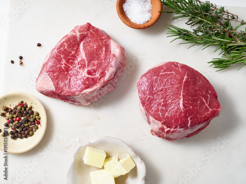 Raw chuck tender steak placed on a marble cutting board with salt, pepper, herbs, and butter ready for cooking in the kitchen