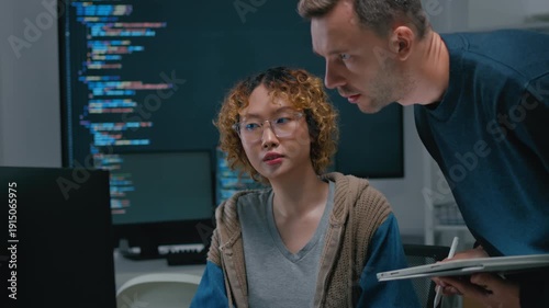 Focused diverse software engineers and AI developers working on code on computer screens in a dark office. Concept of machine learning, digital transformation, and future technology innovation.