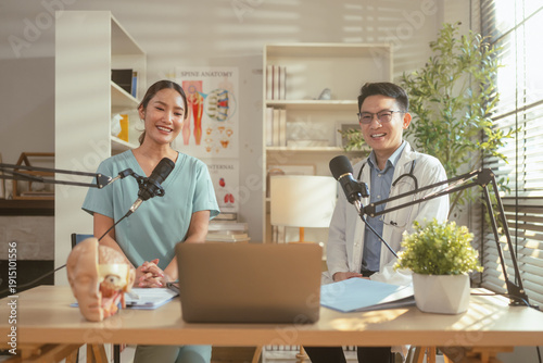 Asian medical doctor hosting a healthcare podcast interview with a nurse inside a bright clinic office. Professional consultation recording with microphones and laptop discussing treatment, patient 