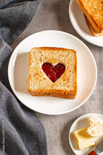Toast with heart cutout filled with strawberry jam on white plate, romantic breakfast concept
