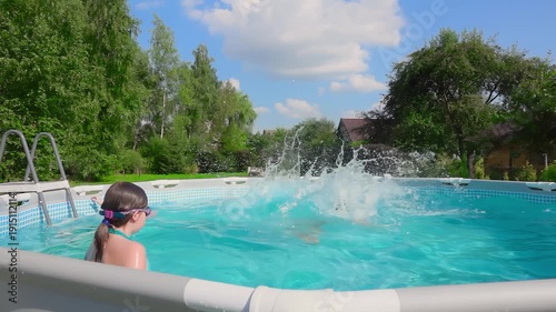 Happy girl in swimsuit jumping into blue frame swimming pool at country house. Summer childhood joy and healthy family lifestyle concept