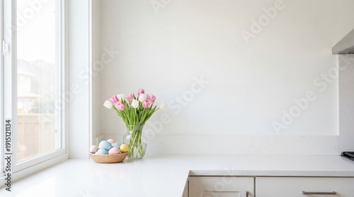 Pastel Easter eggs in bowl with pink tulips on modern kitchen countertop. Bright spring home interior with natural light and copy space.
