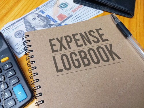Fotografi Brown spiral notebook with Expense Logbook text on a wooden desk with a calculator and dollar bills