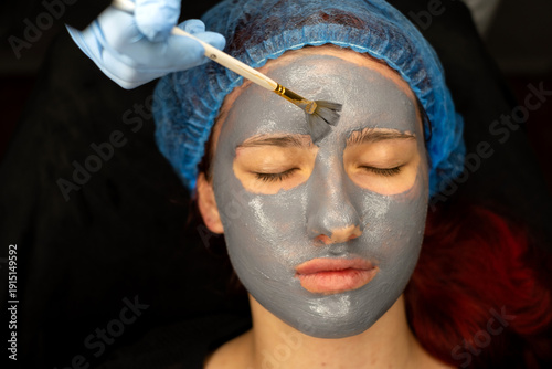 Cosmetologist applying mask on face of woman in spa salon