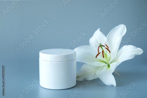 Jar with cream and lilies on light gray background, space for text