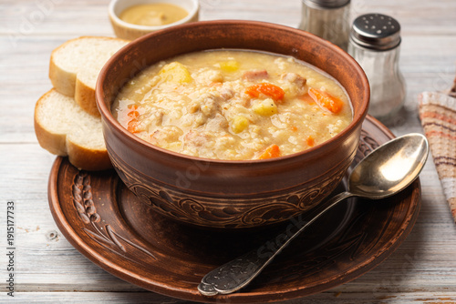 Soup kulesh with millet, potatoes, onion, carrot, meat and bacon in ceramic bowl on wooden background.