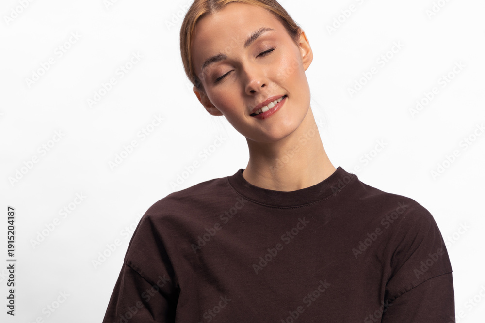 Fototapeta premium Young woman with closed eyes and gentle smile wearing dark sweater on white background. Concept of calm, relaxation, peacefulness, and natural beauty in studio portrait.