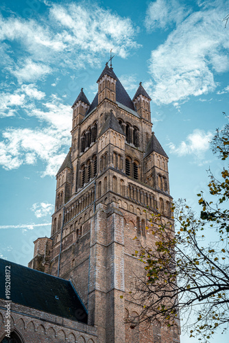portrait shot of old ancient medieval building in bruges brugge in belgium with trees and leaves coming into frame and cloudy blue clear skies above in autumn 