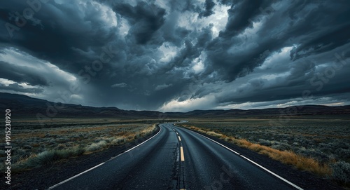 Curved blacktop road stretching across dramatic tundra terrain beneath threatening storm clouds and dark sky