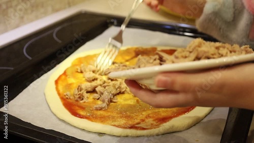 Adorable young girl preparing homemade pizza by placing ingredients on fresh dough. 