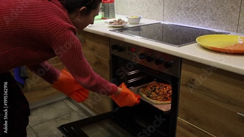 A young woman carefully removes a freshly baked pizza from the oven.