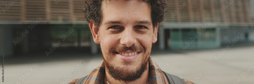 Obraz premium Close up, guy student stands outside the university building looks at the camera and smiles. Panoramic