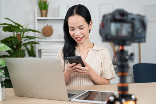 Content Creator Studio: A young woman, engaged in creating content, is seated at a table with a laptop, smartphone and camera, crafting a digital presence