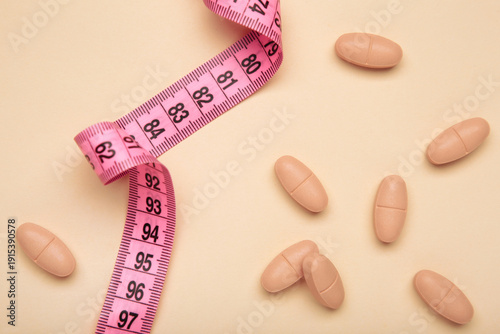 A measuring tape with a variety of colorful pills on beige background. Diet pills, weight loss supplements, and medical dosage control concepts.