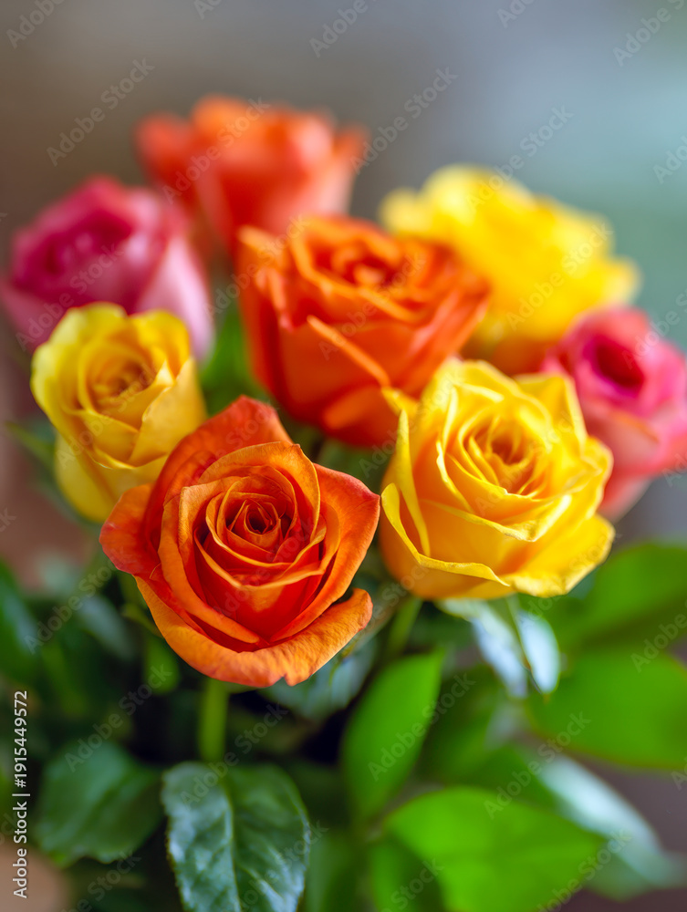 Fototapeta premium Vibrant bouquet featuring a mix of yellow, orange, pink, and red roses with lush green leaves creating a bright and cheerful floral arrangement
