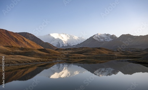 White glaciated and snowy mountain peak Pik Lenin at sunset, mountains reflected in a lake between golden hills, Trans Alay Mountains, Pamir Mountains, Osh Province, Kyrgyzstan