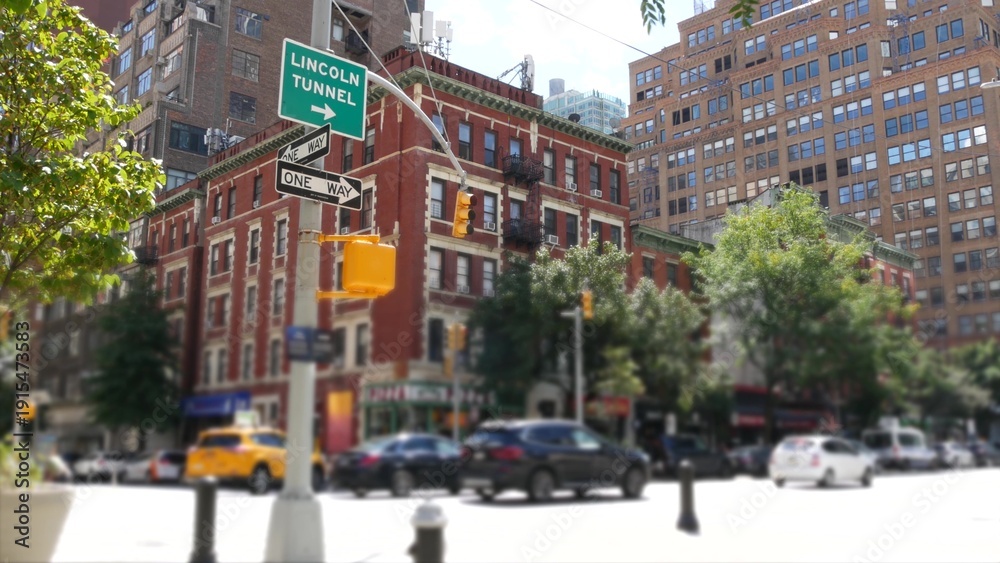 Fototapeta premium Manhattan Midtown street New York City, United States. Red brick house, building architecture in Chelsea residential district. People pedestrian, yellow taxi car on crossroad. Lincoln Tunnel road sign