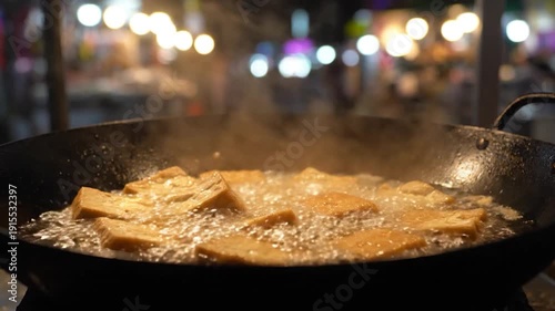 Street food being deep fried in a large wok at night.