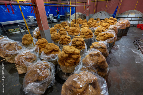 Bogura, Bangladesh - 17 April 2022: View of numerous mounds of golden-brown sweet treats, piled high in baskets, filling a dimly lit room with a warm, inviting glow.