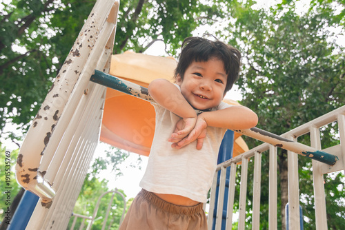 A cute and cheerful little Asian boy as he plays on an outdoor playground. The kid is laughing heartily while enjoying the activities in a public park, a genuine moment of happy childhood