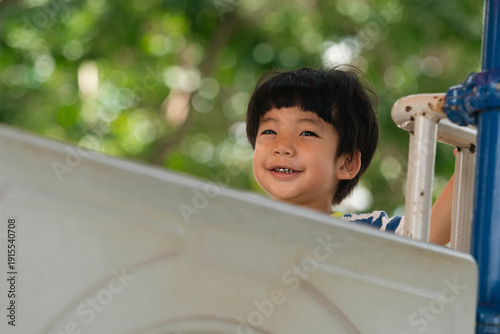 A cute and cheerful little Asian boy as he plays on an outdoor playground. The kid is laughing heartily while enjoying the activities in a public park, a genuine moment of happy childhood