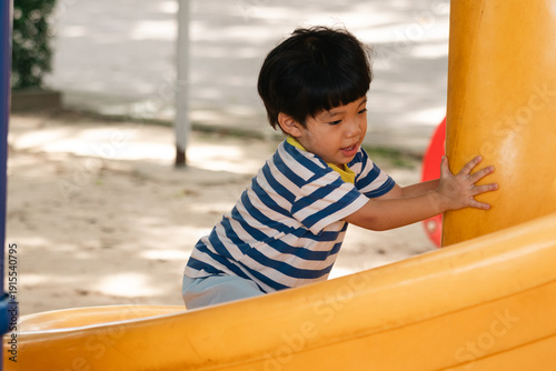 A portrait of a cute and cheerful little Asian boy as he plays on an outdoor playground. The kid is laughing heartily as they enjoy the Slide in a public park, a genuine moment of happy childhood.