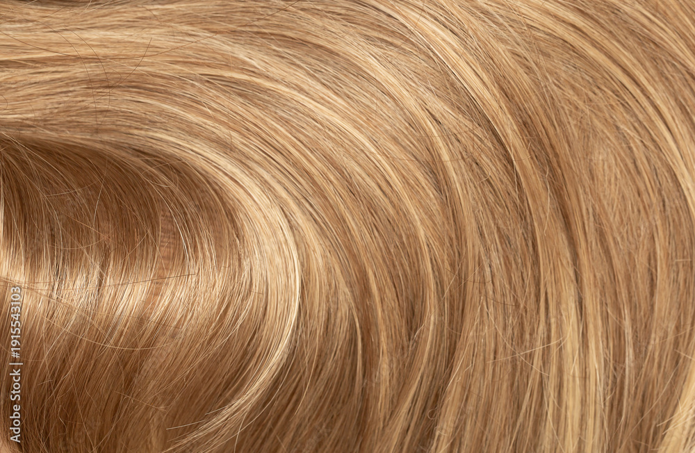 Fototapeta premium Blond hair close-up as a background. Women's long blonde hair. Beautifully styled wavy shiny curls. Hair coloring. Hairdressing procedures, extension.